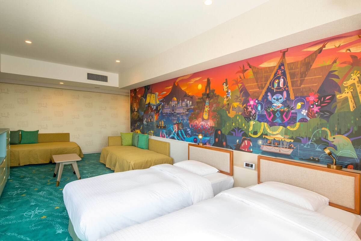 A hotel room with two single beds, a sofa, and a small table. A colorful mural decorates the wall.