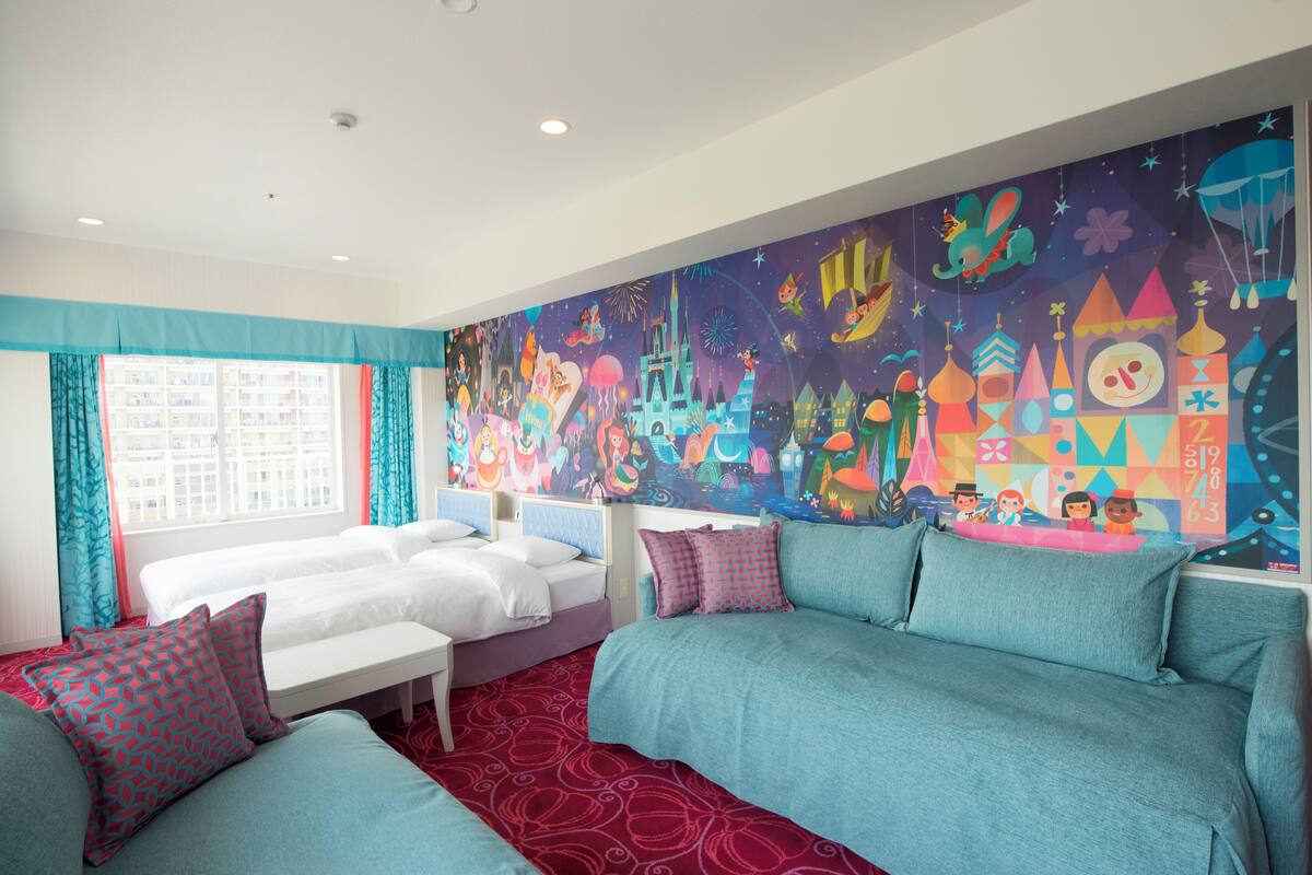 A hotel room with two beds, a sofa, and a colorful mural on the wall.