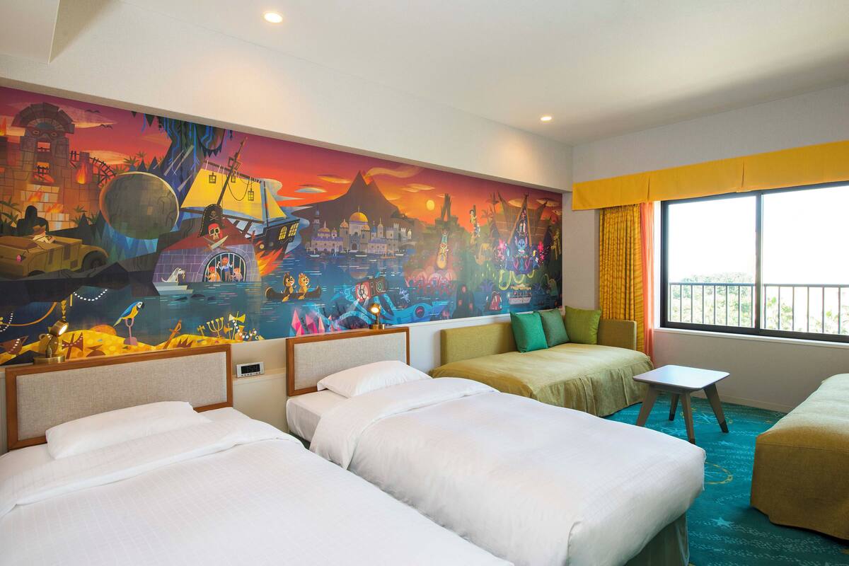 A hotel room with two beds, a small table, and a colorful mural on the wall.