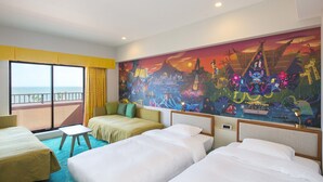 A hotel room with three beds, a small table, and a large window with a view of the sea.