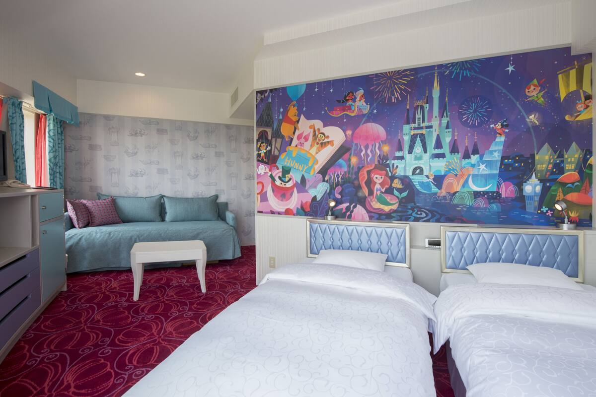 A hotel room with a large mural, a bed, a sofa, and a desk.