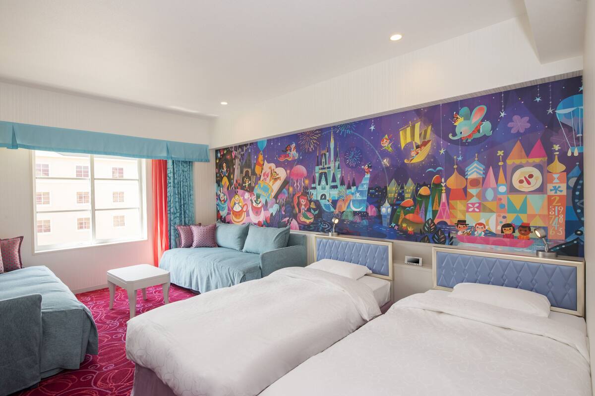 A hotel room with two beds, a small table, and a colorful mural on the wall.
