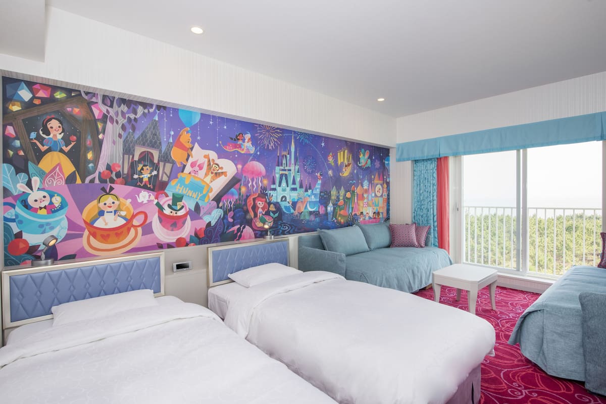 A hotel room with three beds, a large mural, and a balcony with a view.