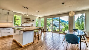 Een moderne keuken met een groot eiland, houten vloeren en grote ramen met uitzicht op een bergachtig landschap.