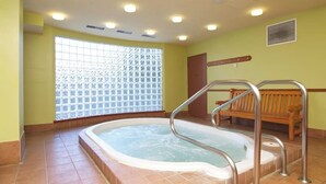 Un cuarto de spa con un jacuzzi, un banco de madera y una ventana con diseño de cuadrícula.