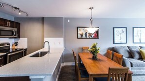 Una cocina moderna con una isla central, un comedor con mesa y sillas de madera, y un sofá gris en la sala de estar.