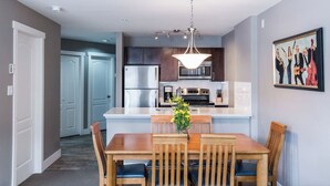Una cocina moderna con electrodomésticos de acero inoxidable, un comedor con mobiliario de madera y una lámpara colgante.
