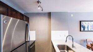 A modern kitchen with a stainless steel refrigerator, a sink, and a wooden chair.