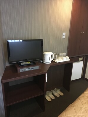 Habitación de hotel con televisión de pantalla plana, cafetera, mini refrigerador y un par de pantuflas en el suelo.