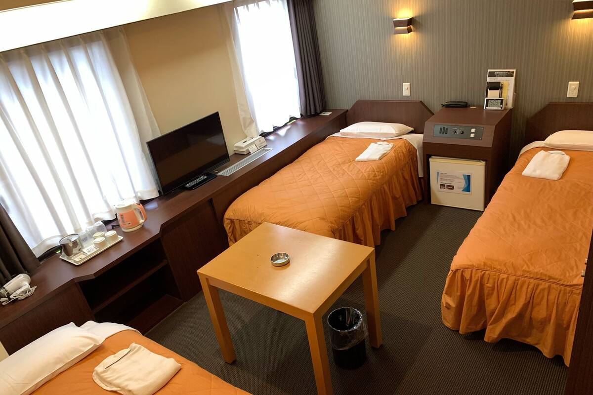 A hotel room with two beds, a desk, a TV, a minibar, and a trash can.