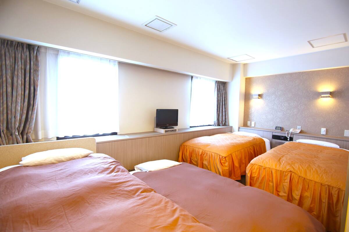 A hotel room with three beds, a television, a desk, and a window with curtains.