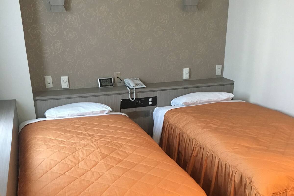 A hotel room with two beds, a bedside phone, and a clock on the wall.