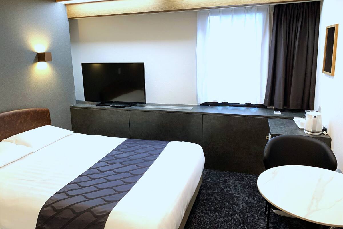 A hotel room with a bed, a television, a desk with a computer, a chair, and a small table.
