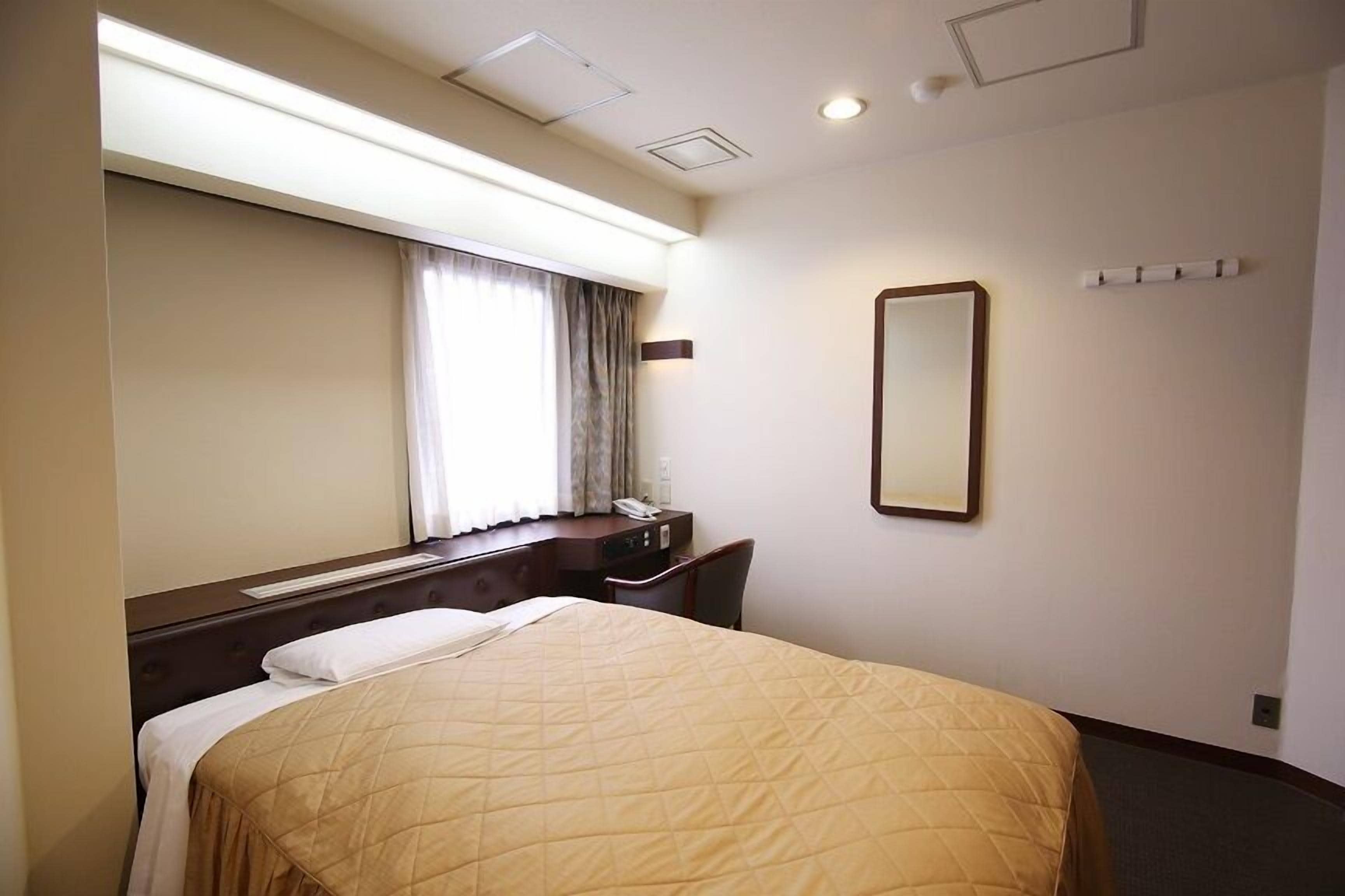 Une chambre d’hôtel avec un grand lit, un bureau, une chaise, un miroir et une fenêtre avec des rideaux.