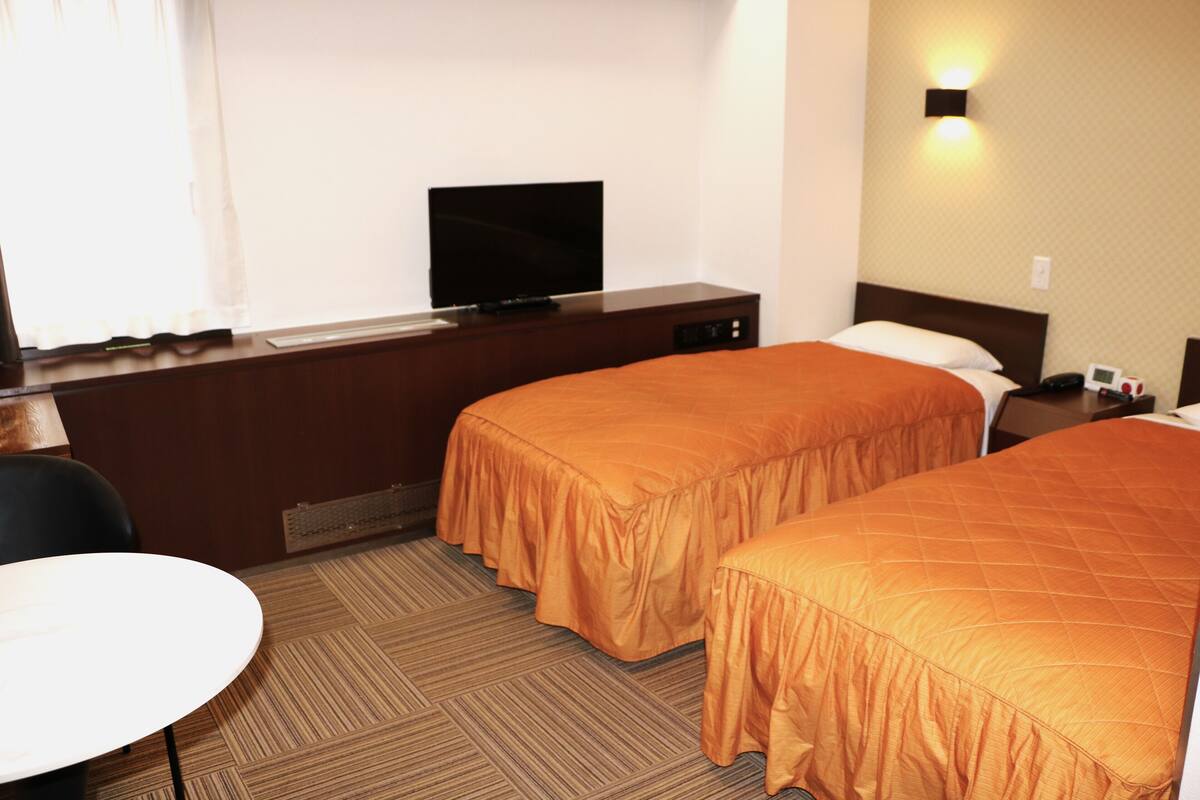 A hotel room with two beds, a television, a desk, and a chair.