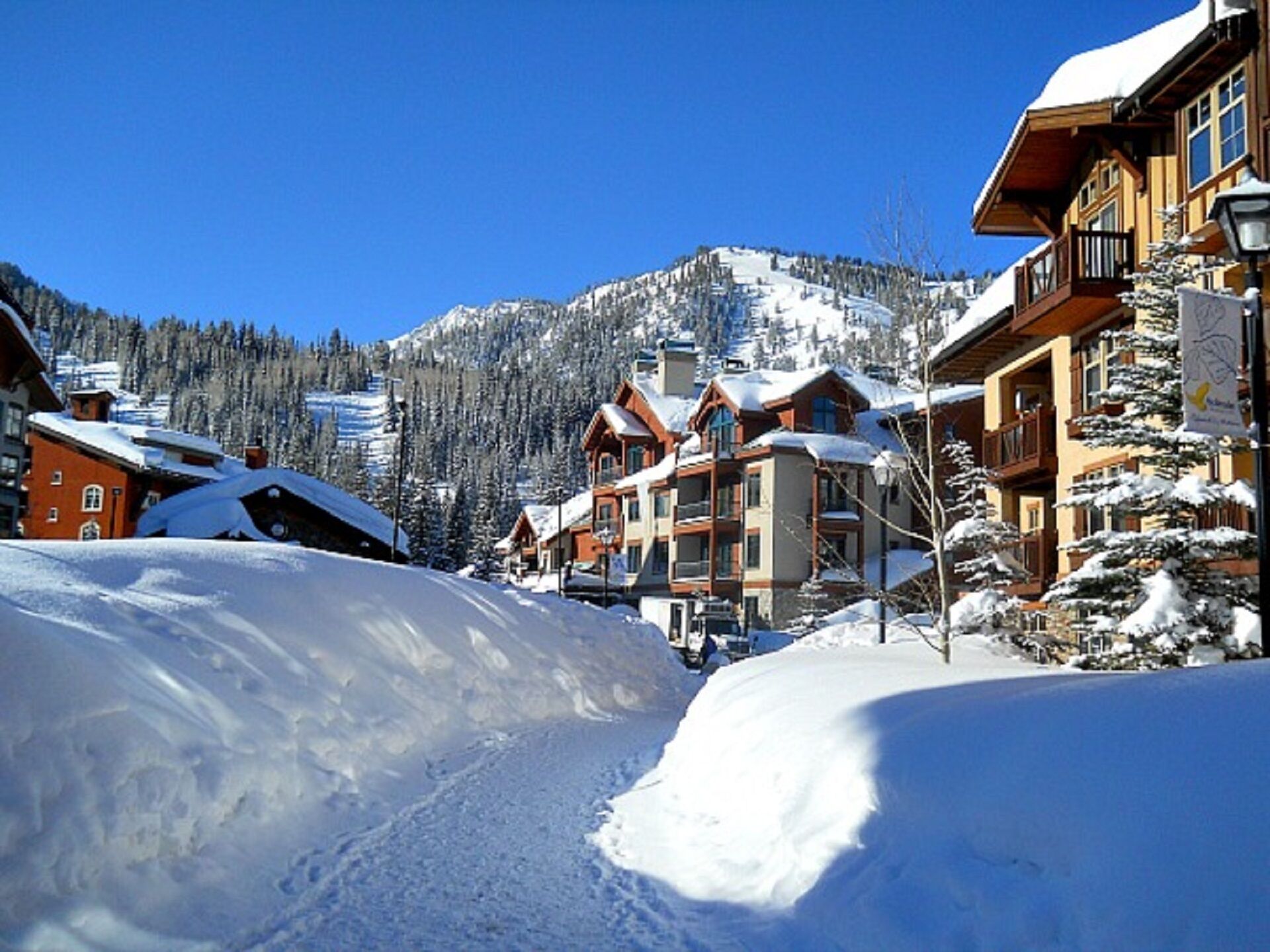 A snow-covered mountain town with wooden buildings and a ski slope in the background.