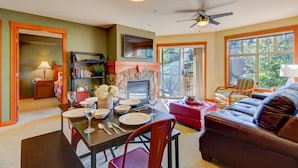 A dining area with a table set for four, a fireplace, and a sofa in a room with large windows and a ceiling fan. - Pristine Ski Retreat, Slope Views in Solitude Village, 2 Bedroom, 2 Bath (Solitude)