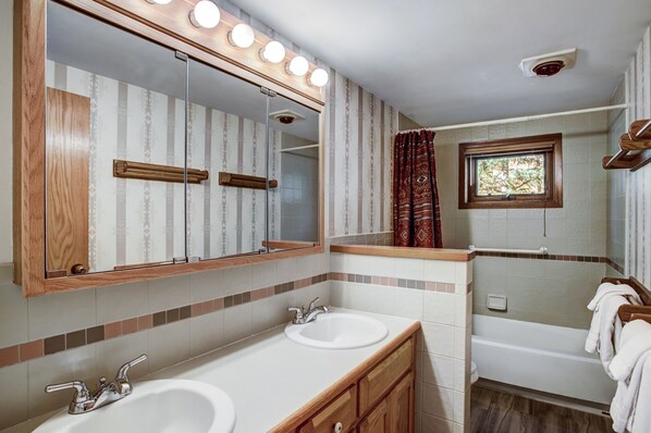 A bathroom with a large mirror, two sinks, a bathtub, and a window.