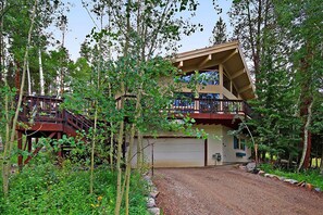 A two-story cabin with a wooden deck and a garage, surrounded by dense forest. - 1 Mile To Lifts, Hot Tub, Great Views, Peaceful Setting, Discount Rates (Breckenridge)