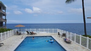 Zona de piscina con vista al océano, sillas de descanso y señal de prohibido sumergirse.
