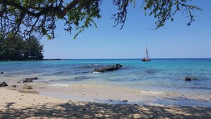 Una playa con agua turquesa cristalina, una orilla arenosa y un velero a lo lejos.