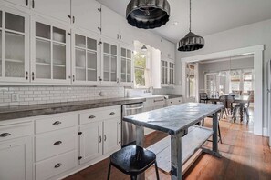 Una cocina con armarios blancos, encimera de mármol y una mesa grande.