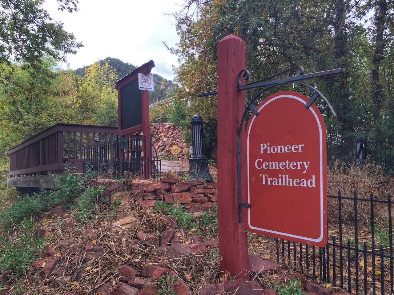 En skylt som markerar starten på vandringsleden genom Pioneer Cemetery, med ett trästaket och en liten byggnad i bakgrunden.