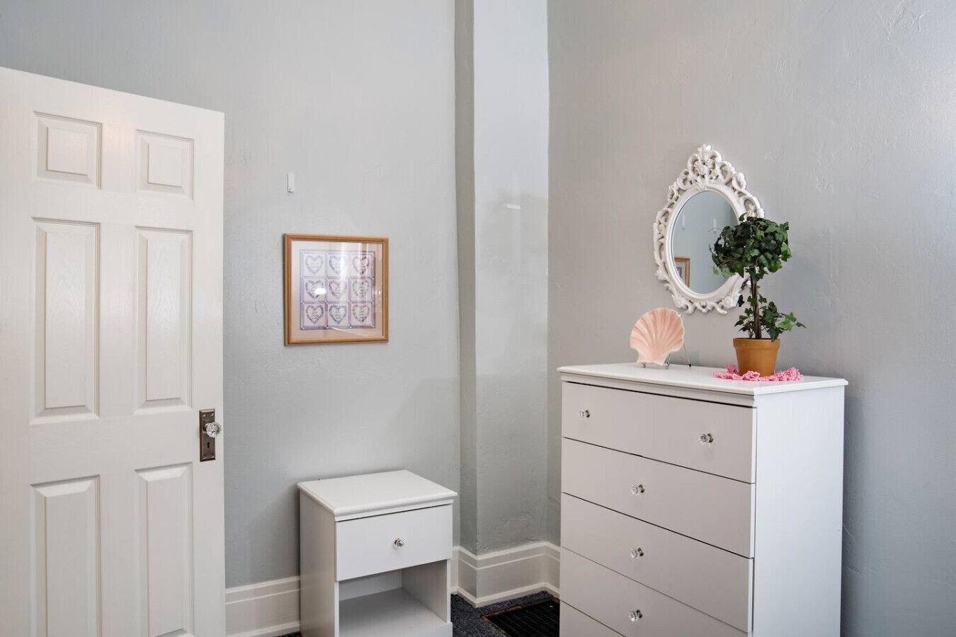 A bathroom with a white vanity, a framed heart decoration, and a potted plant.