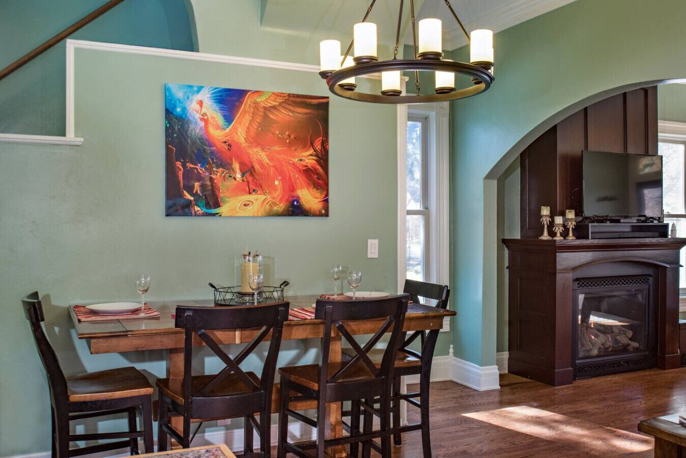 A dining area with a wooden table and chairs, a chandelier, and a fireplace.