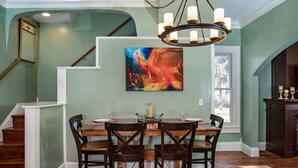 Een eetruimte met een houten tafel en stoelen, een kroonluchter en een schilderij aan de muur.