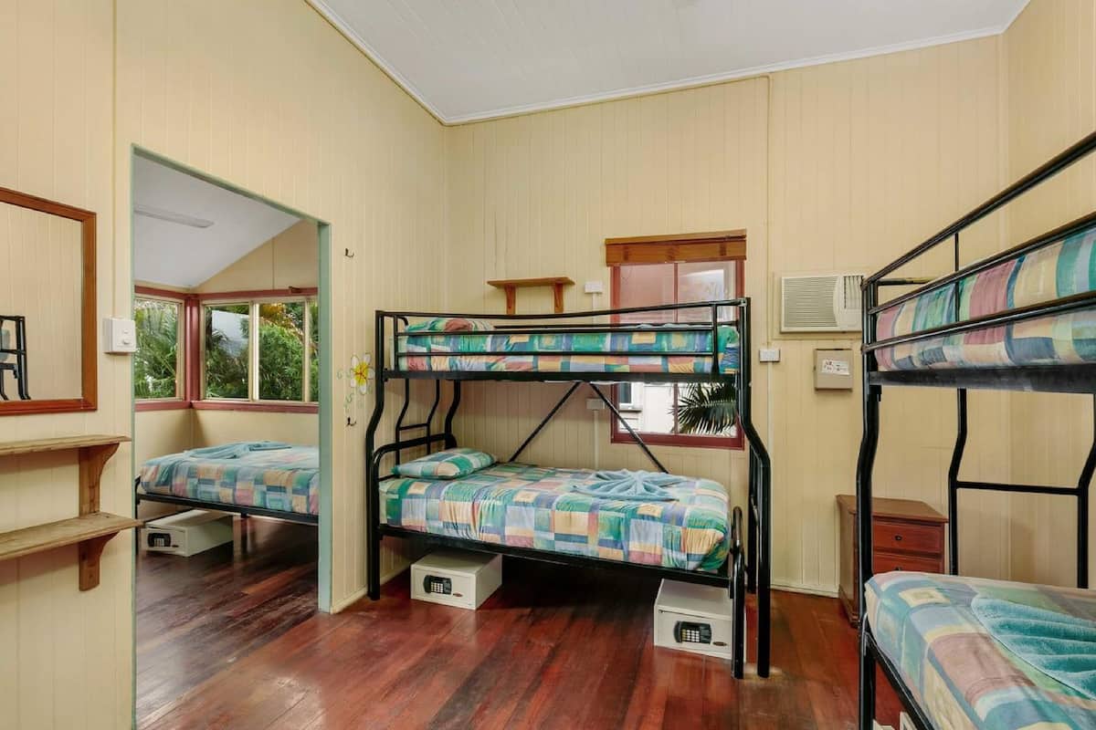 A room with bunk beds, wooden flooring, a window, and a door leading to another room.