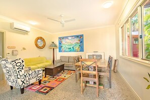 A living room with a yellow sofa, a patterned armchair, a wooden dining table, and a colorful rug. - Travellers Oasis - Hostel (Parramatta Park)