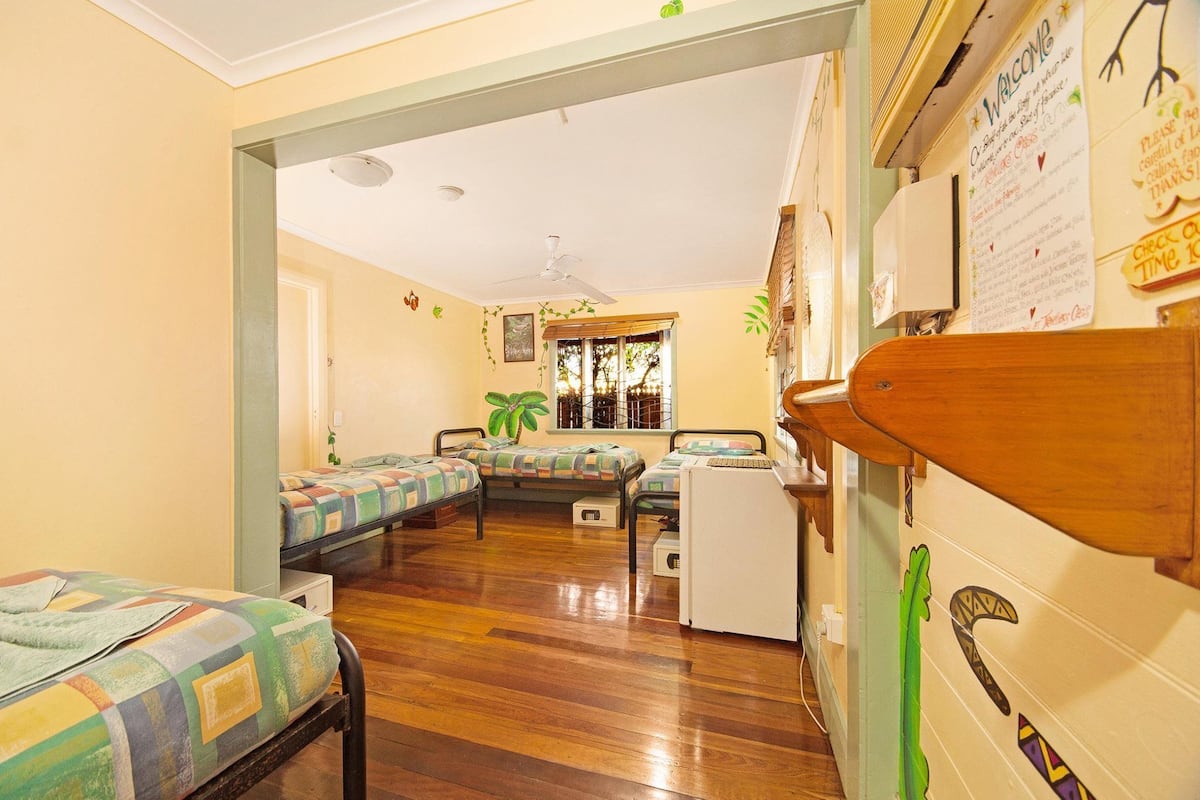 A room with wooden flooring, bunk beds, a desk, and a window with blinds.