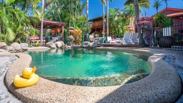 Un espace piscine avec des chaises longues, un flotteur en forme de canard et des palmiers.