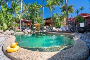 A pool area with lounge chairs, a duck float, and palm trees. - Travellers Oasis - Hostel (Parramatta Park)
