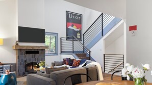 Ein modernes Wohnzimmer mit Kamin, einer Sofagarnitur, einem Esstisch mit Brot und einer Treppe mit Geländer.