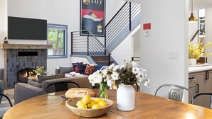 Ein modernes Wohnzimmer mit Kamin, einem Esstisch mit Zitronenschale und Blumenvase, einer Couch und einer Treppe mit schwarzer Geländer.