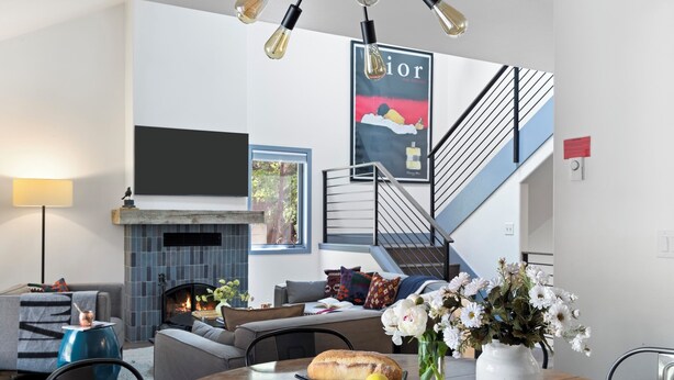 Ein modernes Wohnzimmer mit Kamin, einem Esstisch mit Zitronen und Blumen, einer Couch und einer Treppe.