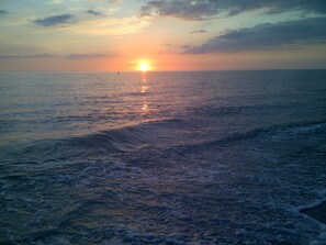 Una playa con el sol poniéndose en el horizonte.