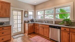 A modern kitchen with wooden cabinets, a dishwasher, and a large window with a view of greenery. - Historic Downtown Home with Private Heated Pool! Walk to Everything!  (St Augustine)
