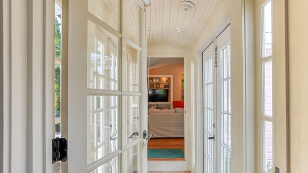 A hallway with a wooden ceiling, white doors, and a view into a living area with a television, sofa, and red chair. - Historic Downtown Home with Private Heated Pool! Walk to Everything!  (St Augustine)