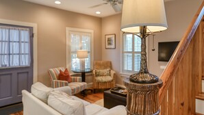 A living room with a white sofa, a striped armchair, a wooden floor lamp, and a ceiling fan. - Historic Downtown Home with Private Heated Pool! Walk to Everything!  (St Augustine)
