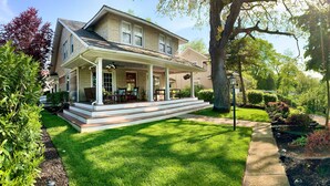 Une maison à deux étages avec un porche à l’avant, un étang et une pelouse bien entretenue.
