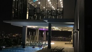 A modern hotel with a rooftop pool area, large windows, and a view of the cityscape at night.
