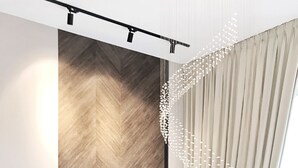 A modern interior with a herringbone wood floor, a large window with curtains, and a decorative chandelier.