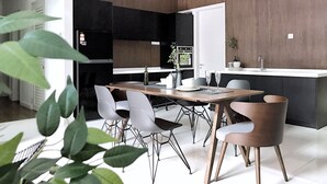 A modern kitchen with a dining area, featuring a wooden table, white chairs, and a built-in oven.