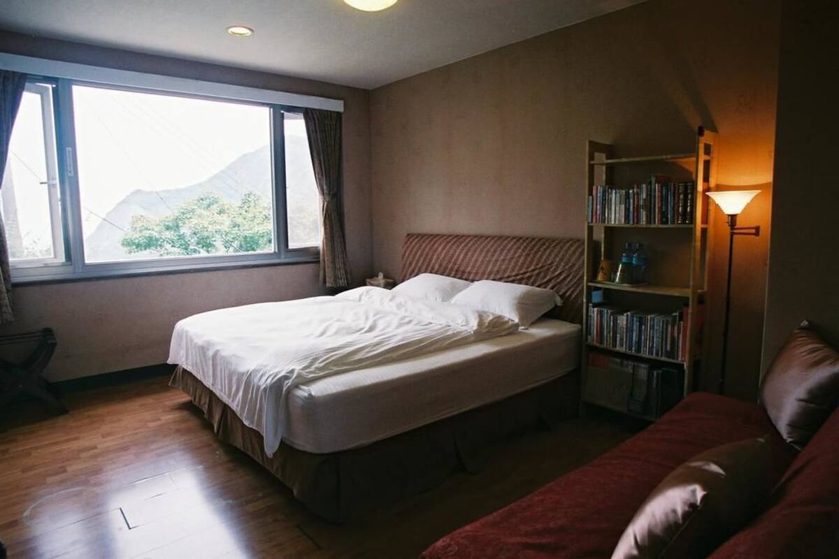 A hotel room with a bed, a bookshelf, a couch, and a window with a view of mountains.
