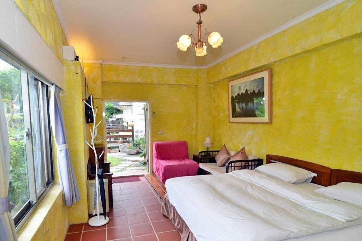 A room with two beds, a chair, a table, and a painting on the wall.