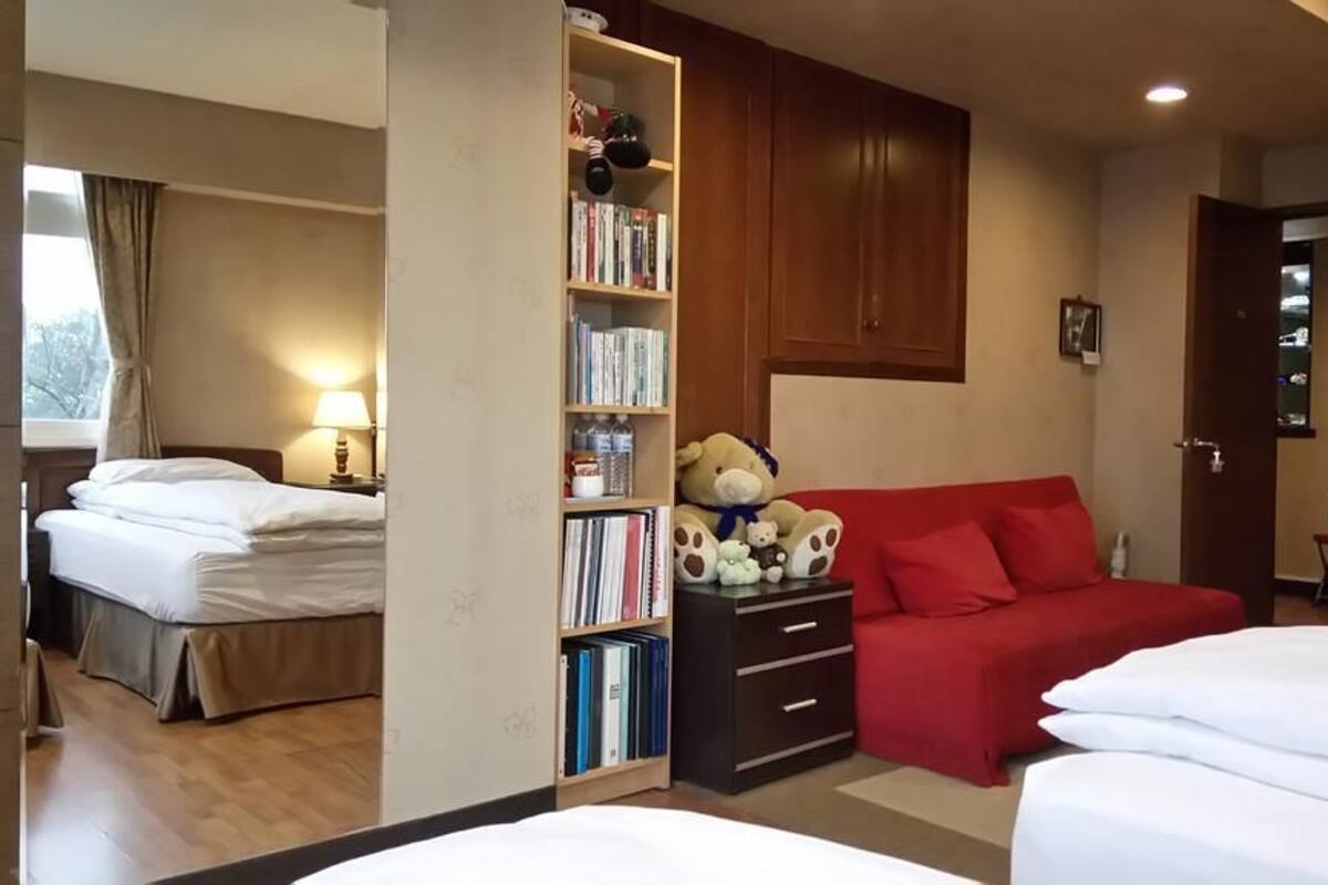 A hotel room with a bed, a red sofa, a bookshelf, and a teddy bear.