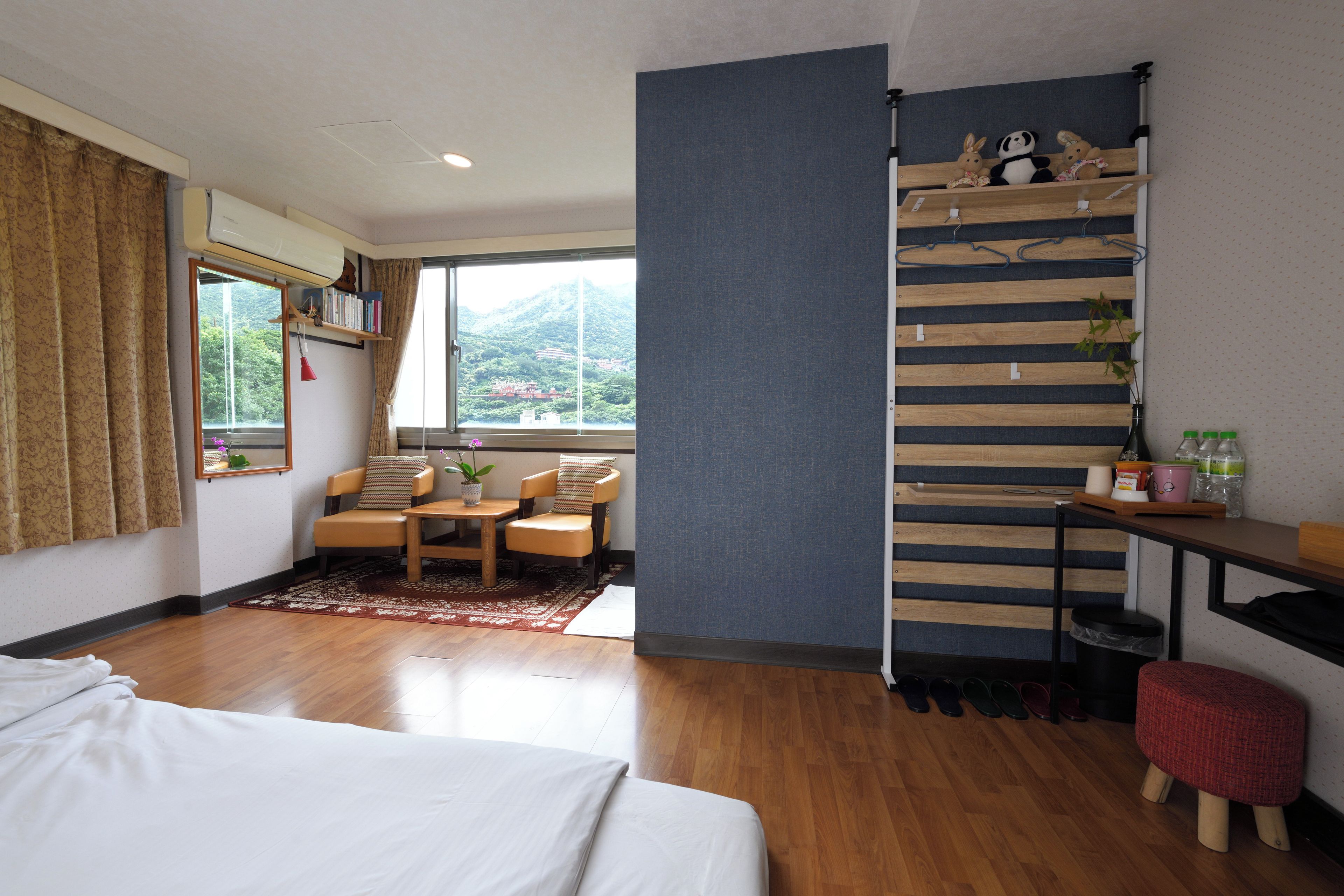 A hotel room with a bed, a desk, a chair, a window with a view of mountains, and a shelf with stuffed animals.